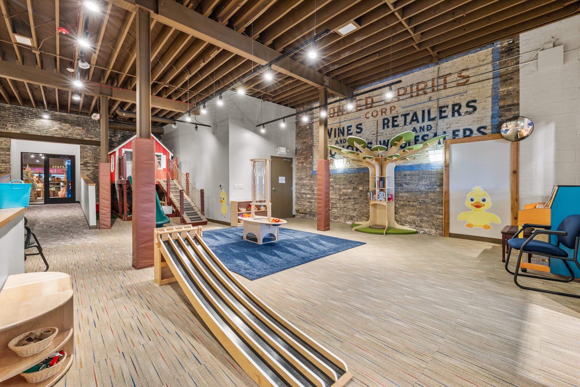 The main room of the Six Little Ducks indoor play space in downtown Oconomowoc, with a wooden ball run and reading tree bookshelf