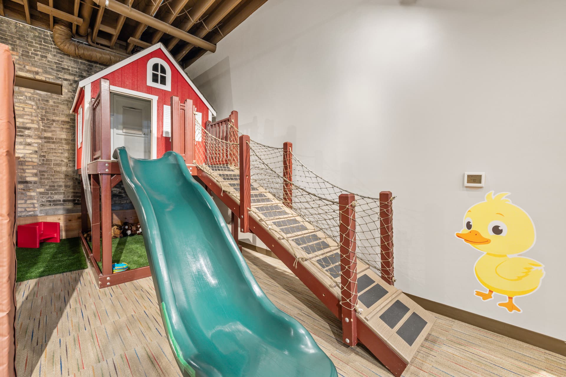 Red playhouse barn with a big green slide and rope bridge at the Six Little Ducks play place in downtown Oconomowoc